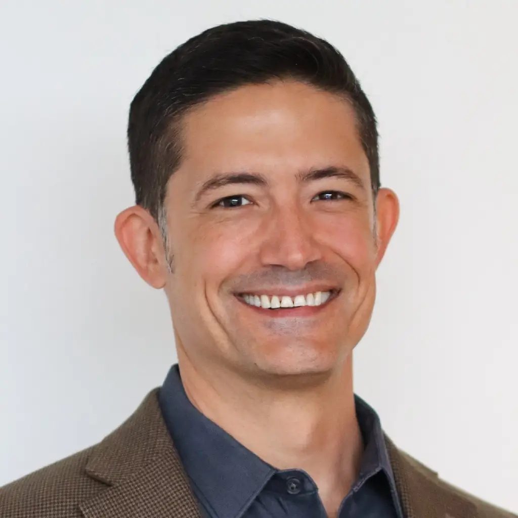 Headshot of the IT manager, smiling in a brown blazer and dark shirt.