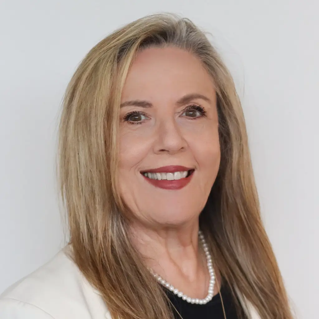 Client services executive headshot, smiling in a white blazer and pearl necklace.